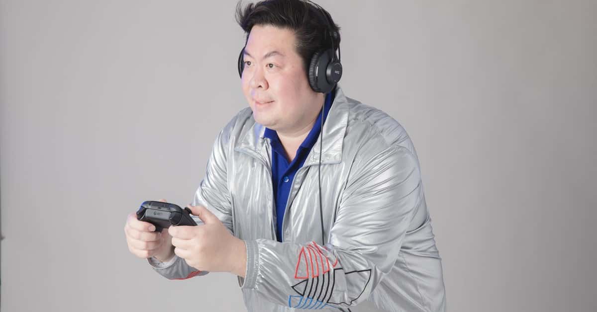A man wearing headphones and a silver jacket engrossed in playing video games indoors.