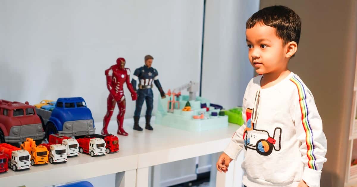 Young boy playing with toy cars and action figures at home.