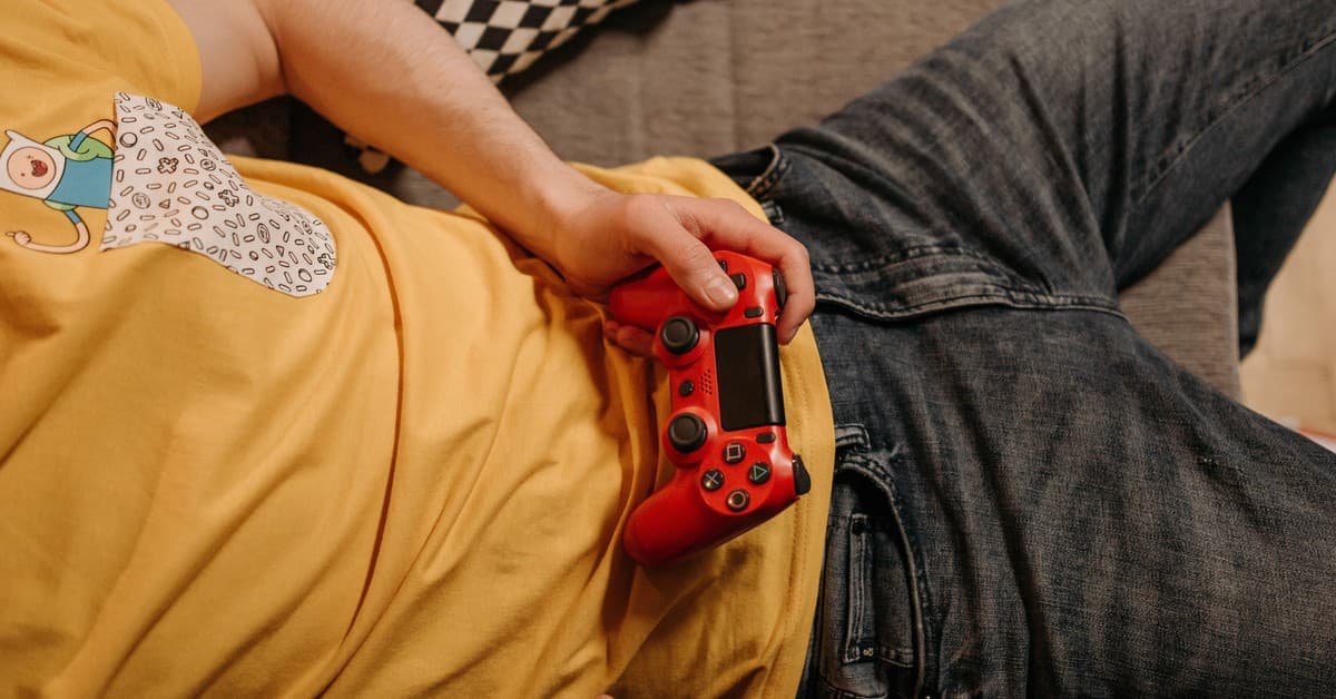 Person holding a red game controller while relaxing on a couch in comfortable clothes.