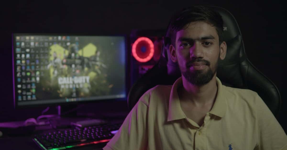 A bearded man sitting at a computer setup with a gaming PC and chair, creating a moody ambiance.