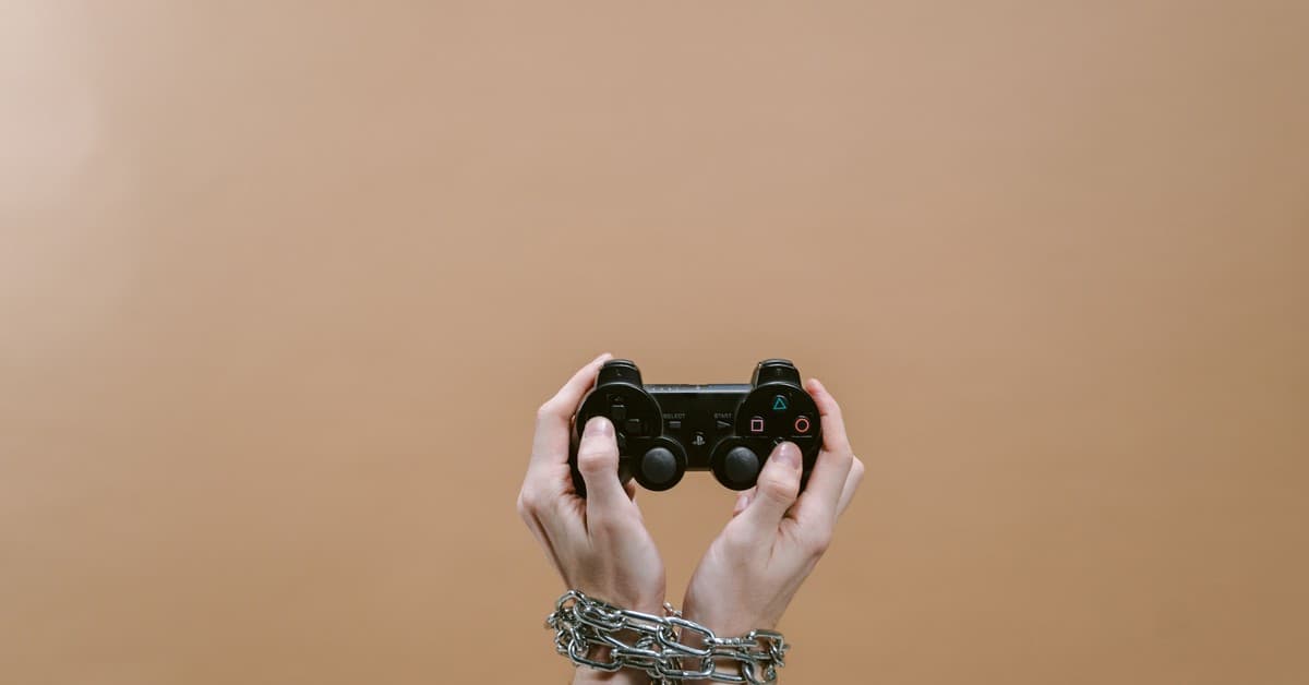 Conceptual image of hands in chains holding a game controller symbolizing gaming addiction.