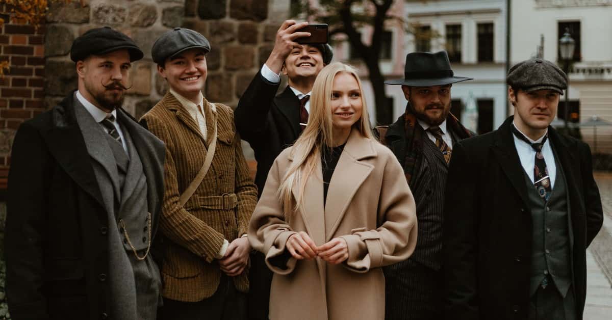 A stylish group in vintage attire and newsboy caps posing outdoors in an urban scene.