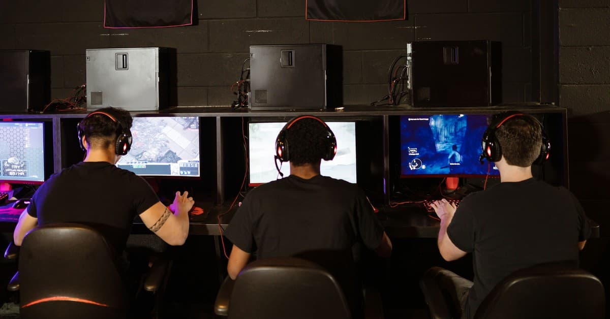 Three men focused on an intense PC gaming session in a modern esports arcade, enjoying teamwork and strategy.