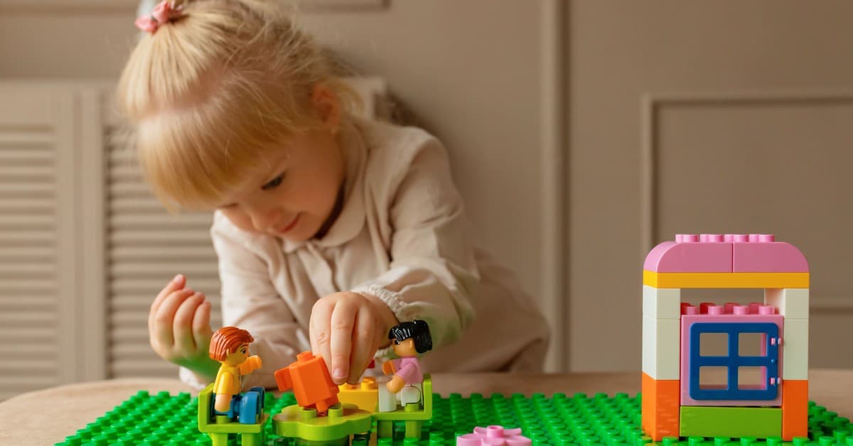 A young girl engaging creatively with colorful plastic building blocks on a table indoors.