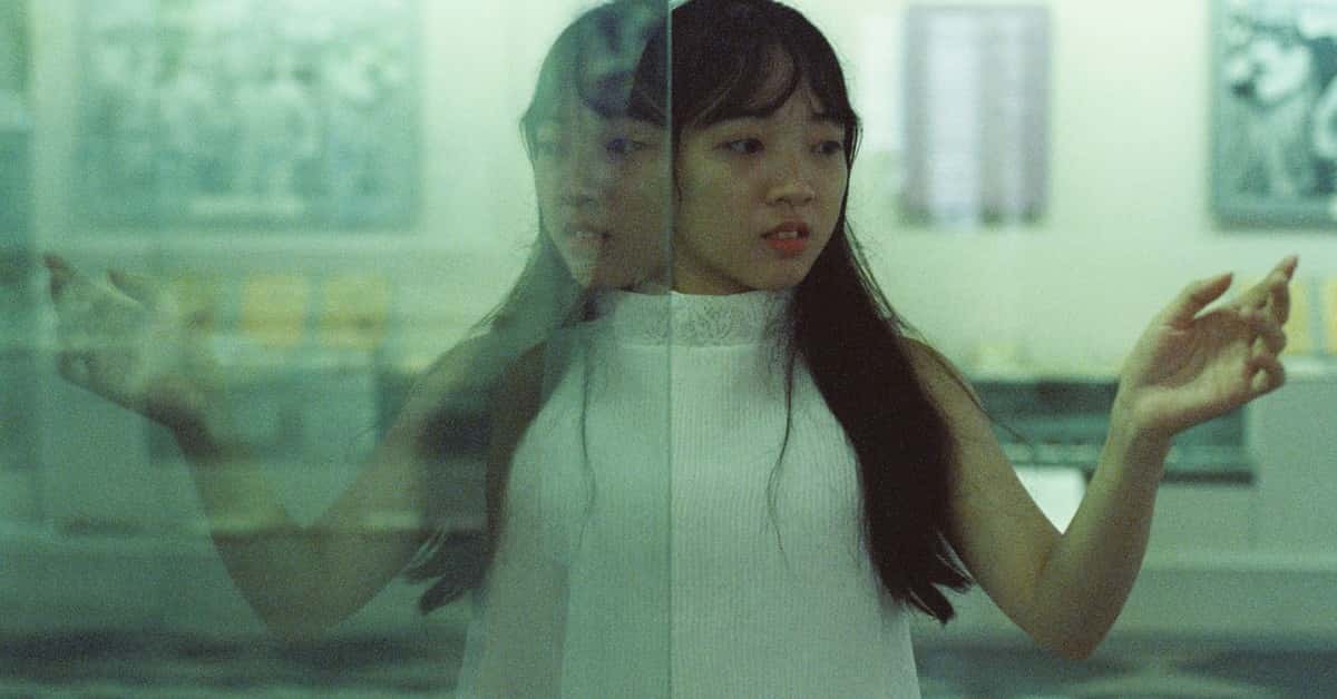 A woman gazes at her reflection in a glass surface, creating an artistic and introspective moment.