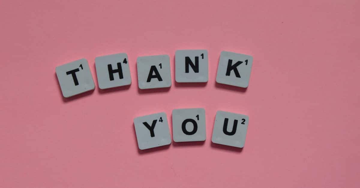 Scrabble tiles forming 'Thank You' on a pink background, ideal for gratitude concepts.