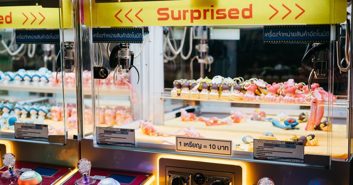 Colorful toys in an arcade claw machine labeled 'Surprised' with vibrant lighting.