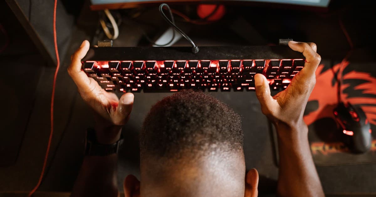 Gamer expresses frustration with video game by holding up keyboard. Overhead shot of gaming setup.