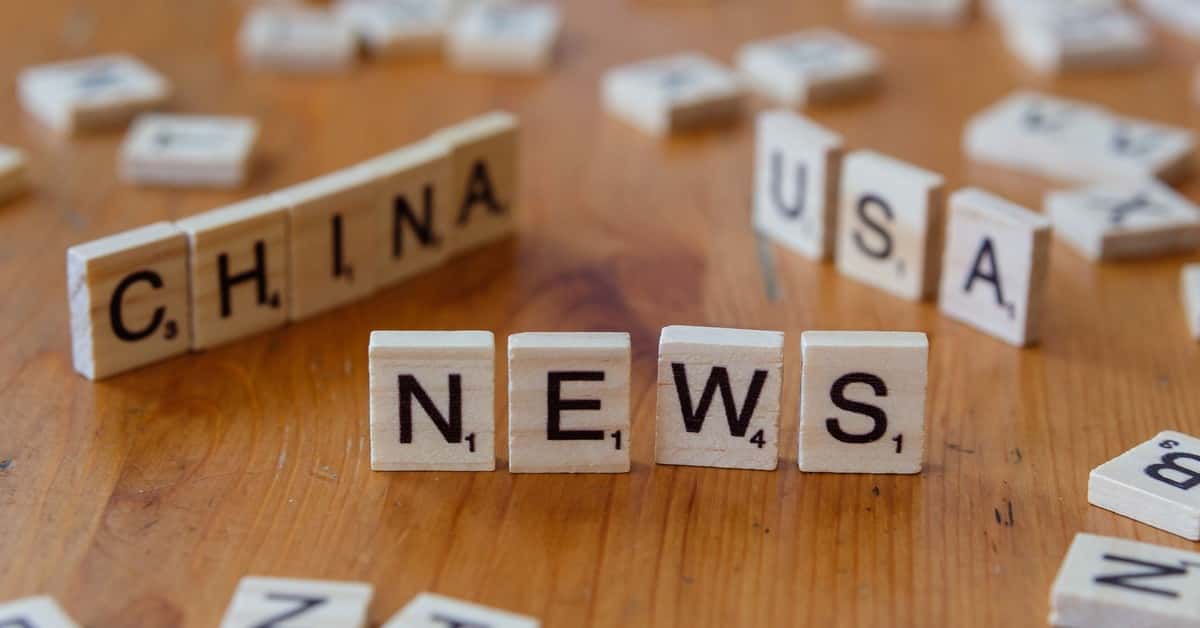 Wooden Scrabble tiles spelling 'NEWS' with 'CHINA' and 'USA' on a wooden surface.
