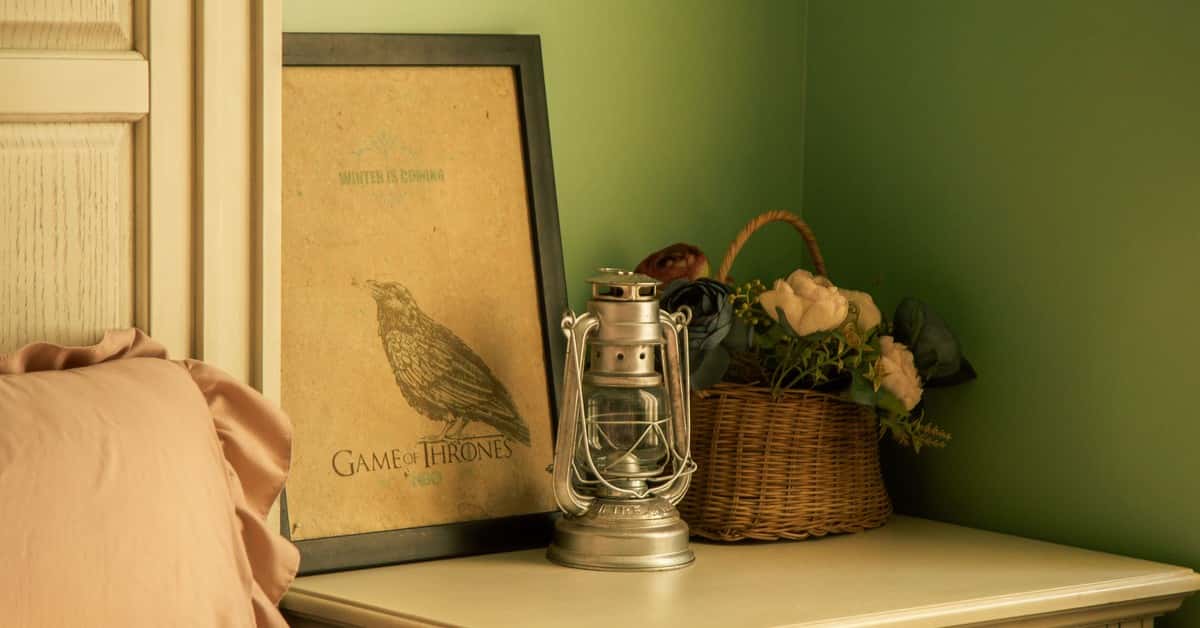 Warmly lit bedroom corner with poster, lantern, and floral basket adding vintage charm.