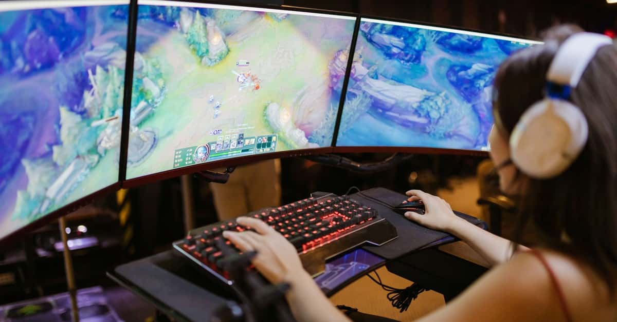 A young woman intently gaming on a multi-screen setup, showcasing vibrant gaming visuals.