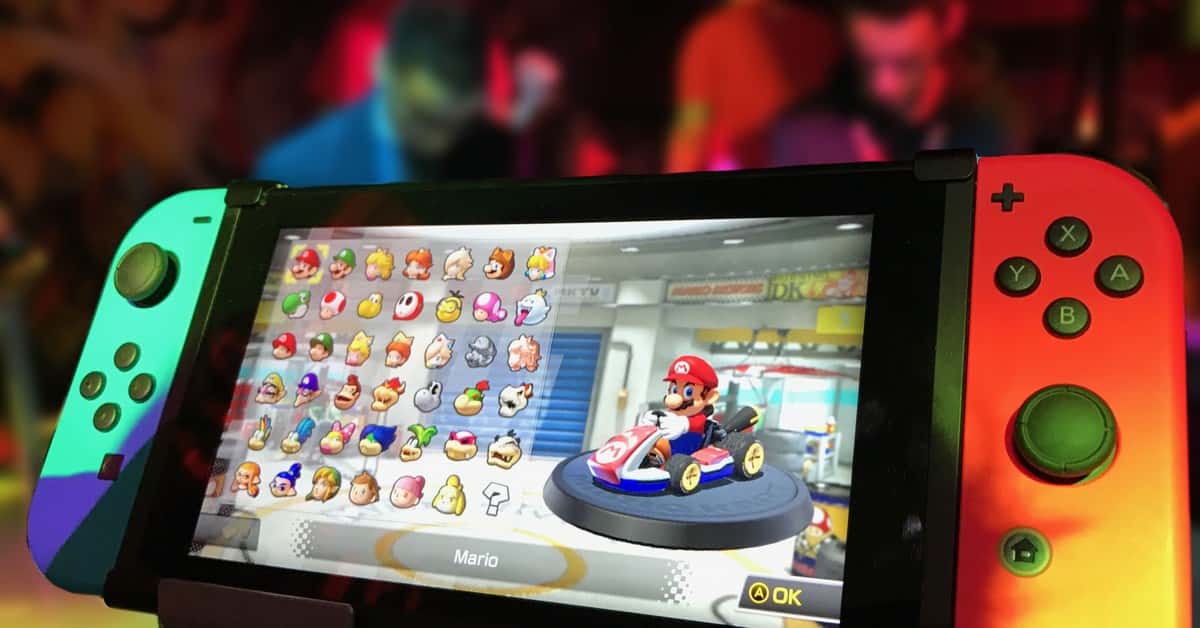 Close-up of a Nintendo Switch showing Mario Kart selection screen, gaming atmosphere in the background.