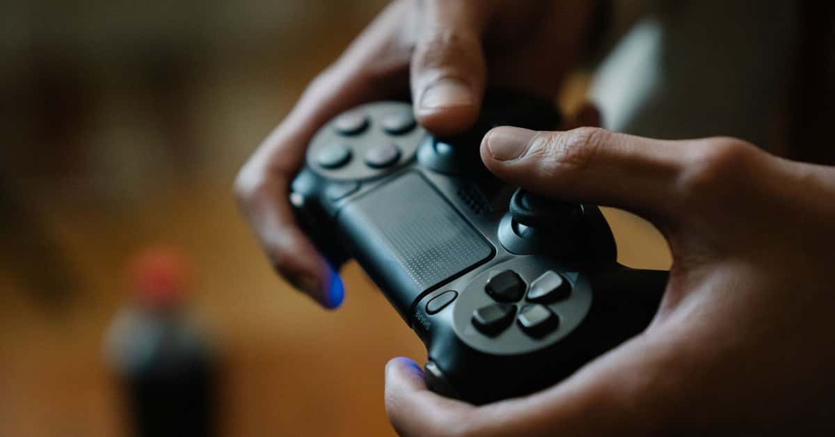 Crop anonymous male pressing buttons on console controller while playing video game in house on blurred background