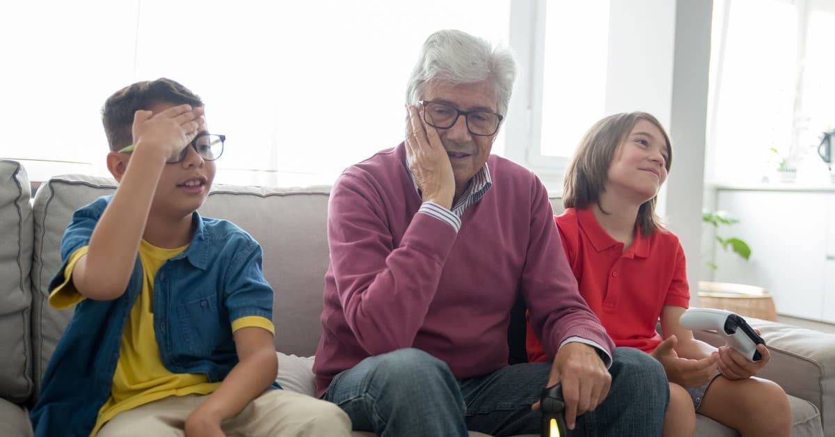 A multigenerational family enjoys playing video games together on a cozy sofa indoors.