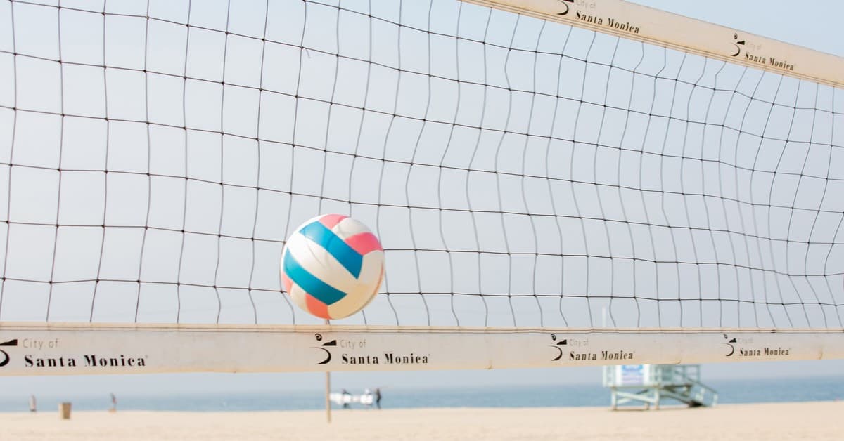 Colorful volleyball in mid-air at Santa Monica beach with net in foreground.