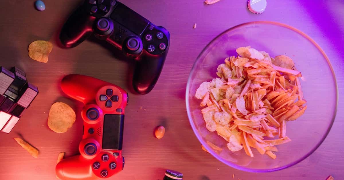 Overhead view of game controllers and snacks on a table, perfect for a gaming night setup.