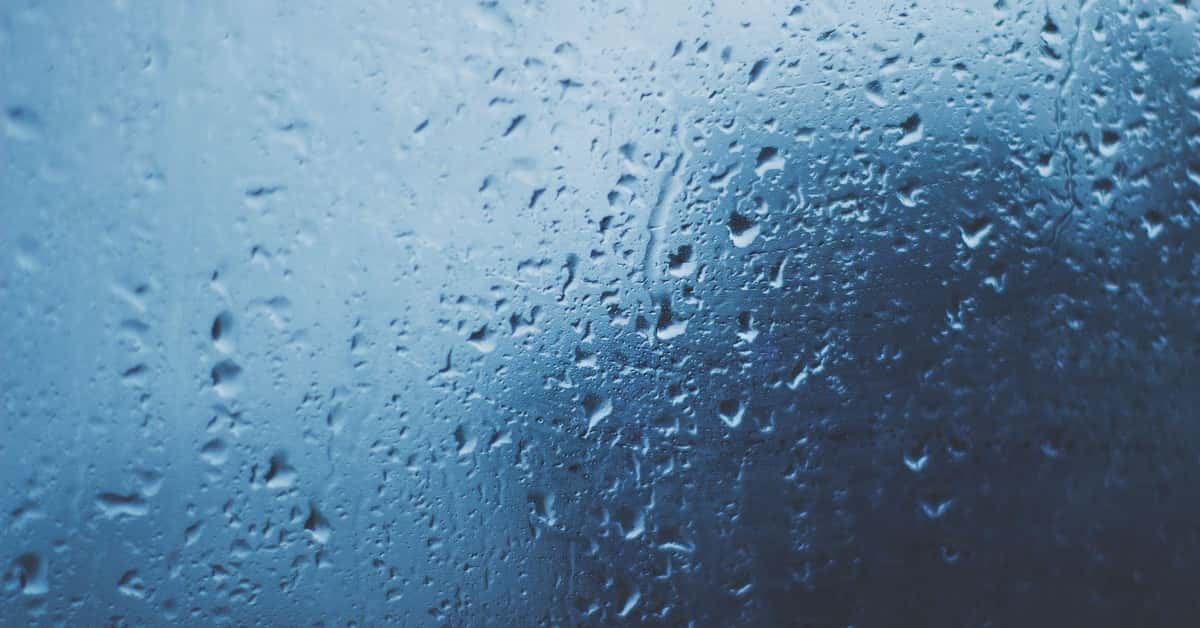 Detailed view of water droplets on a glass window with a blue background.