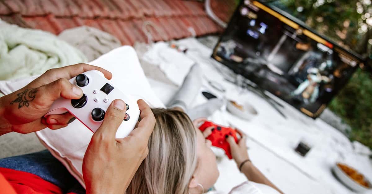 A couple playing video games outdoors, focusing on the controllers and screen.