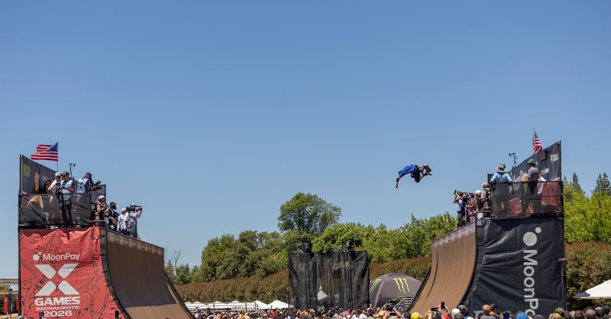 A skateboarder launches off a ramp in mid-air during a vibrant X Games event.