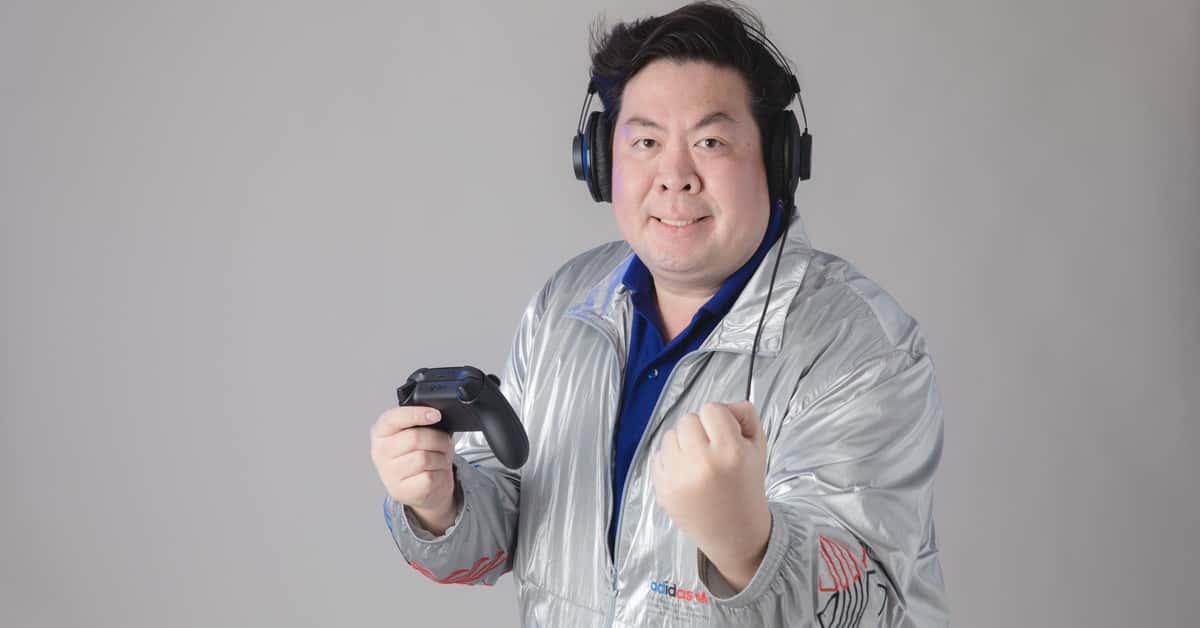 Asian man with headphones celebrates while gaming, holding a controller.