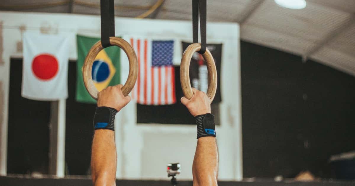 A gymnast performs on rings indoors, showcasing strength and skill.