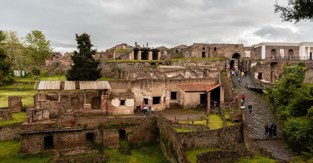 Explore ancient ruins of Pompeii under cloudy skies, capturing rich historical details and lush greenery.