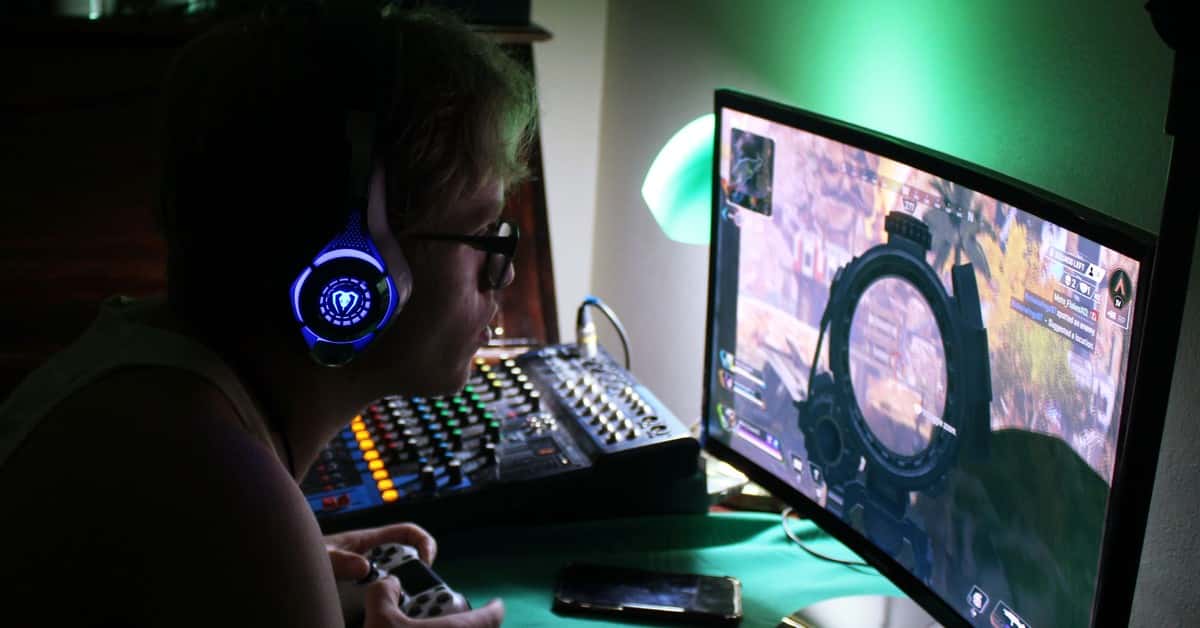 A dedicated gamer using a headset and controller while engrossed in a game, illuminated by green lights.