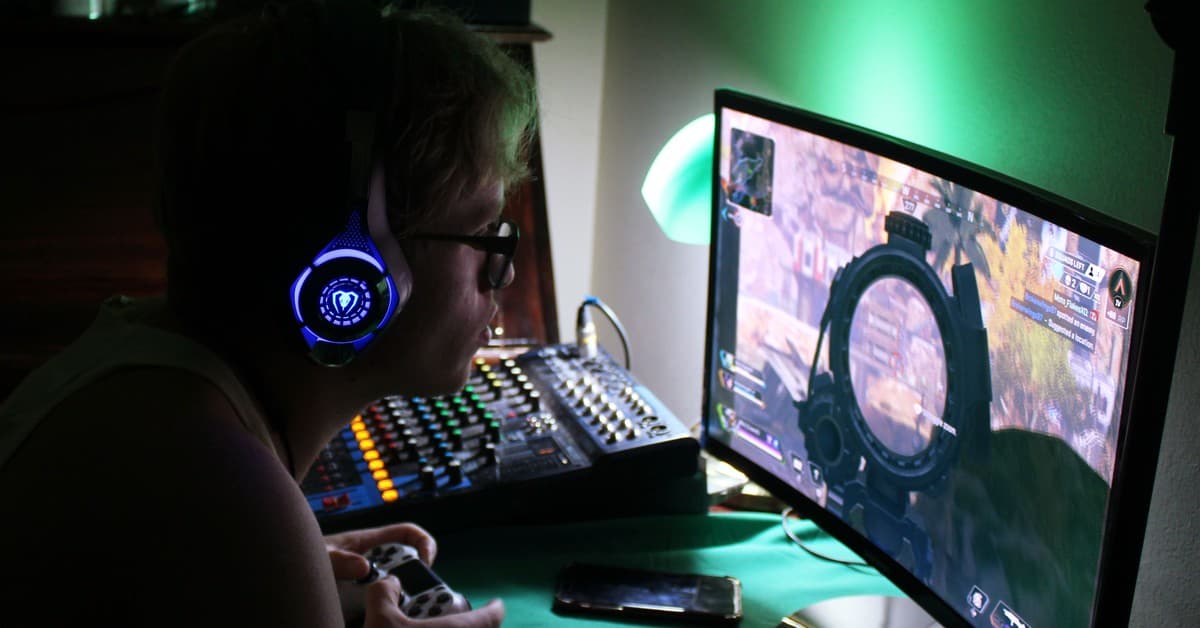 A dedicated gamer using a headset and controller while engrossed in a game, illuminated by green lights.