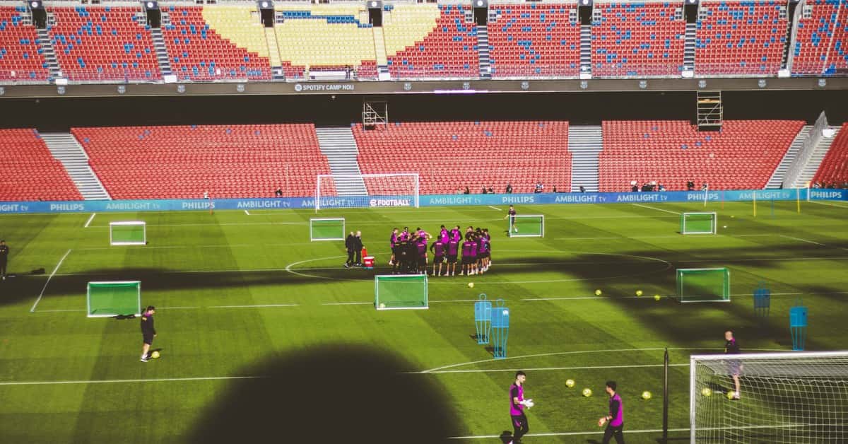 Football team training in a large empty stadium with vibrant red and blue seats.