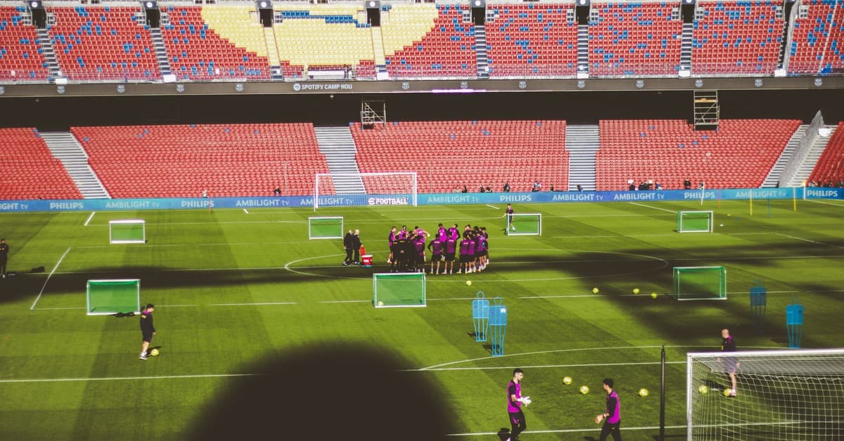 Football team training in a large empty stadium with vibrant red and blue seats.