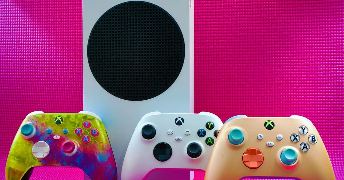 Vibrant gaming controllers displayed with a console on a bold pink backdrop.