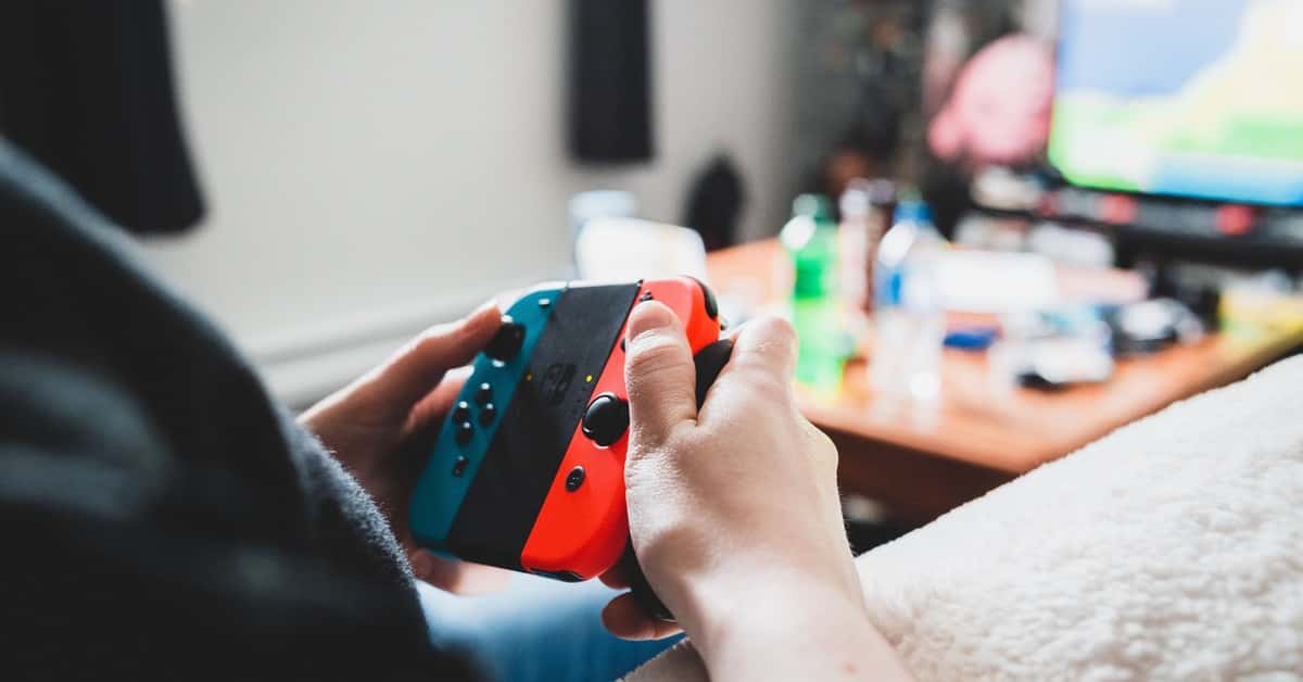 Crop unrecognizable person using console in hands while playing videogame on blurred background