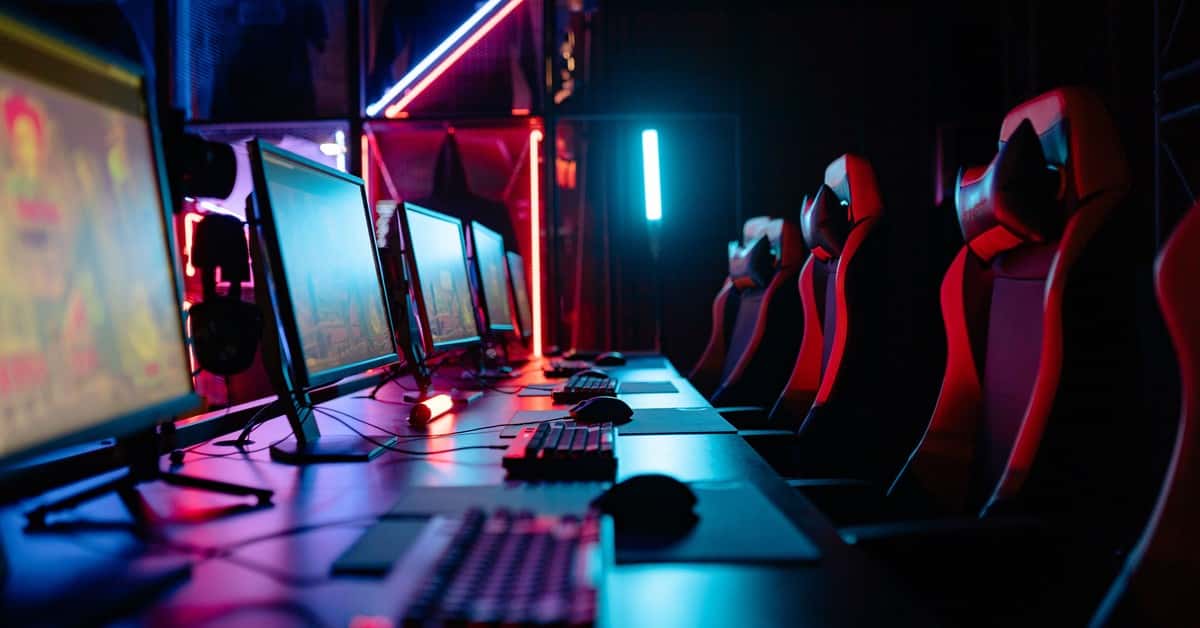 An immersive gaming room with neon lights, computers, and gaming chairs ready for a tournament.