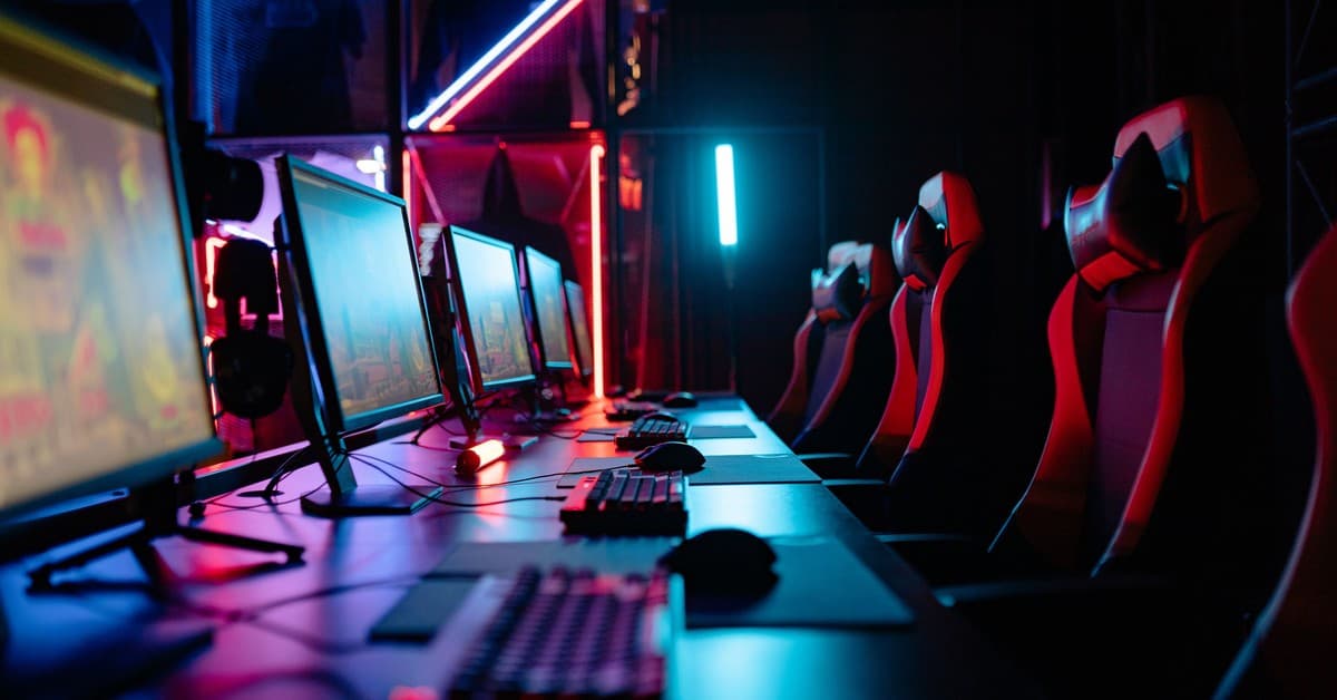 An immersive gaming room with neon lights, computers, and gaming chairs ready for a tournament.