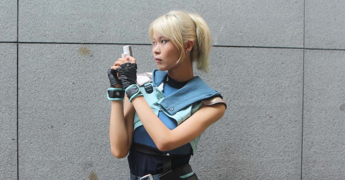 Young woman in futuristic cosplay outfit holding a blaster, posing against a neutral background.