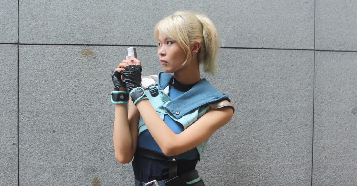 Young woman in futuristic cosplay outfit holding a blaster, posing against a neutral background.