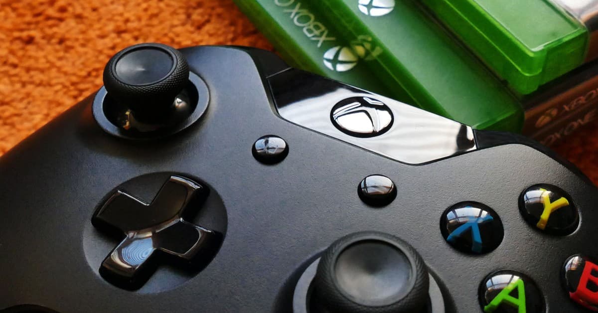 Xbox controller close-up with game cases on orange background.