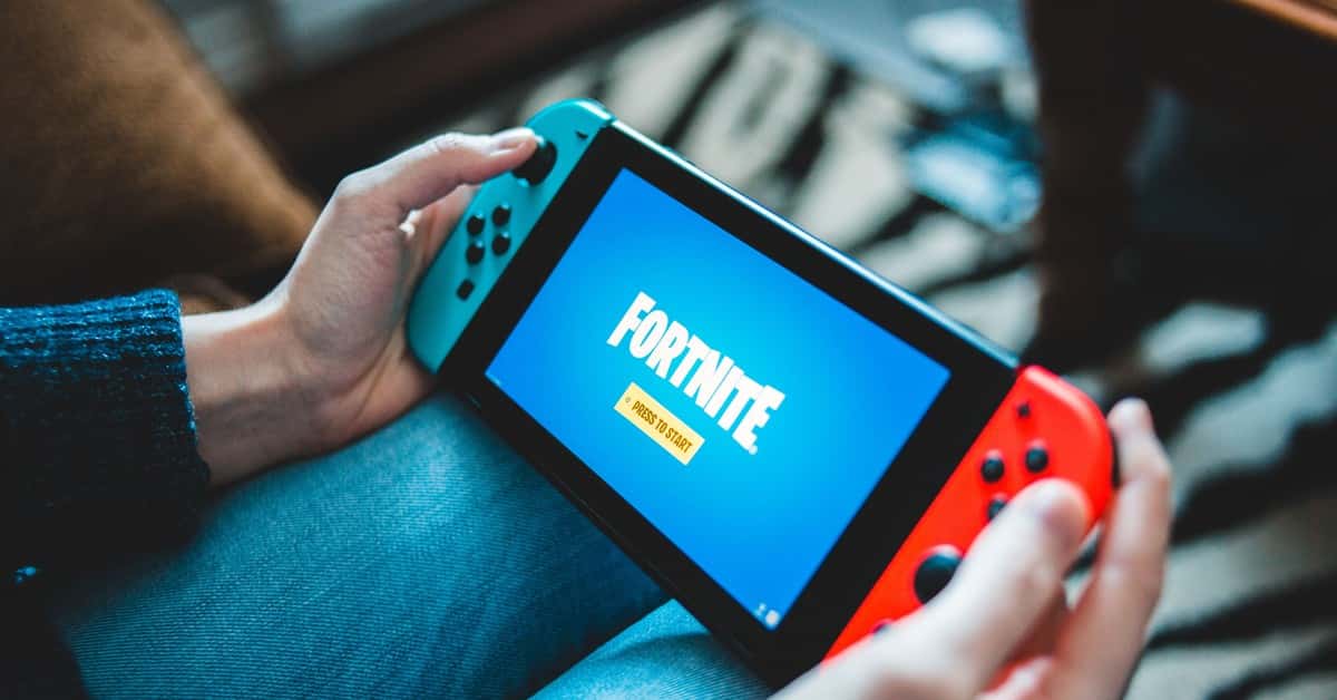 Close-up of hands holding a Nintendo Switch with Fortnite game screen indoors.