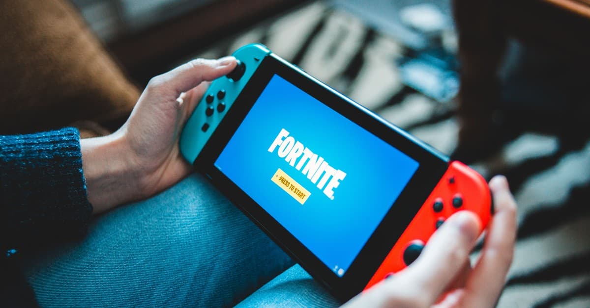 Close-up of hands holding a Nintendo Switch with Fortnite game screen indoors.