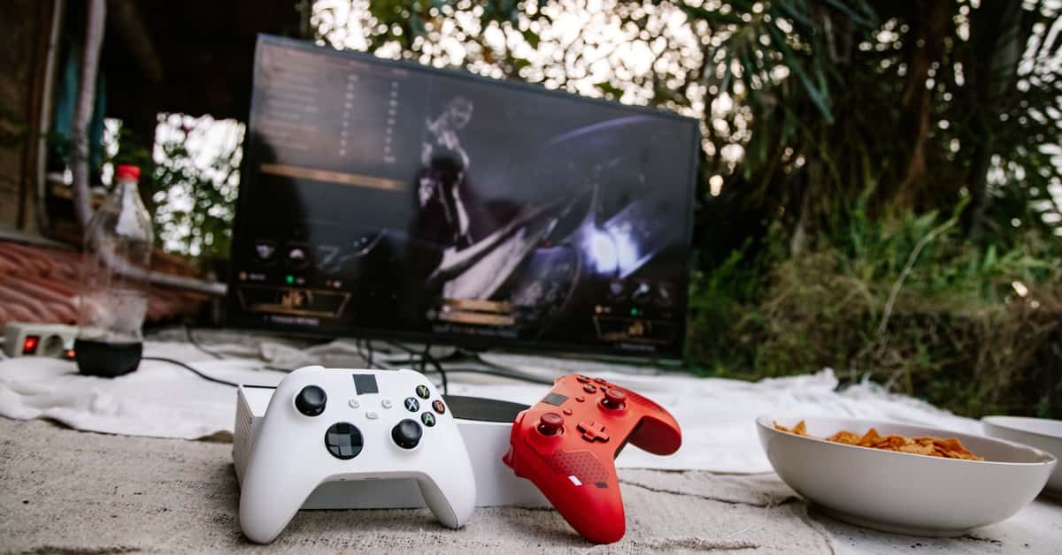 Outdoor gaming scene with controllers on a mat and a screen showing a video game.