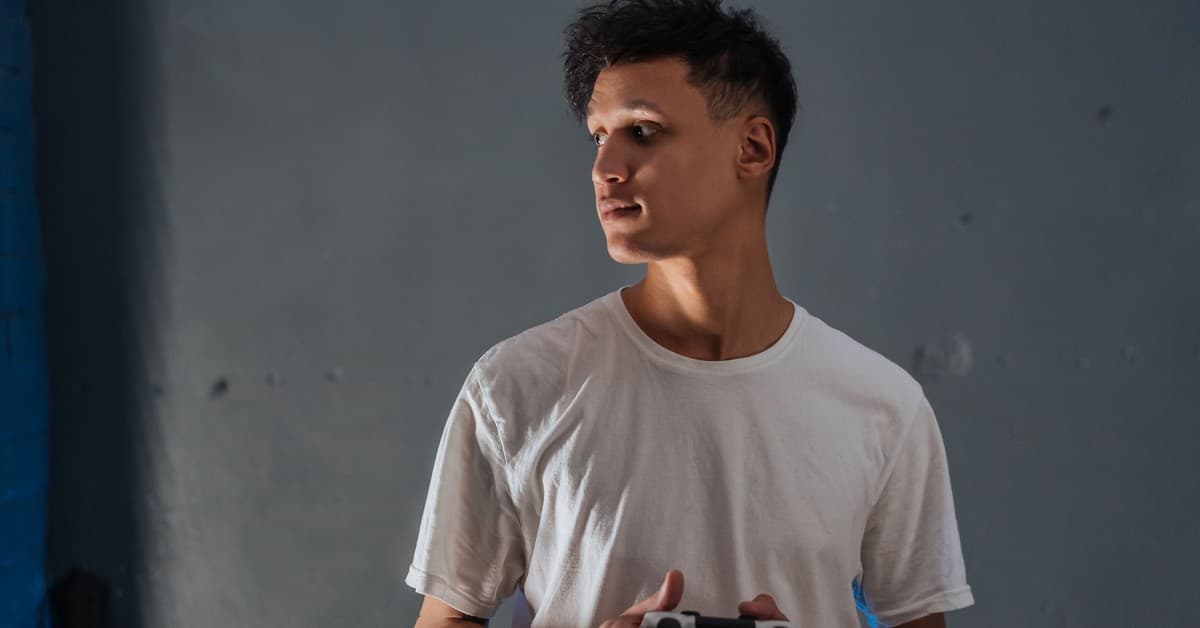 A young man wearing a white t-shirt focuses intently while holding a game controller indoors.