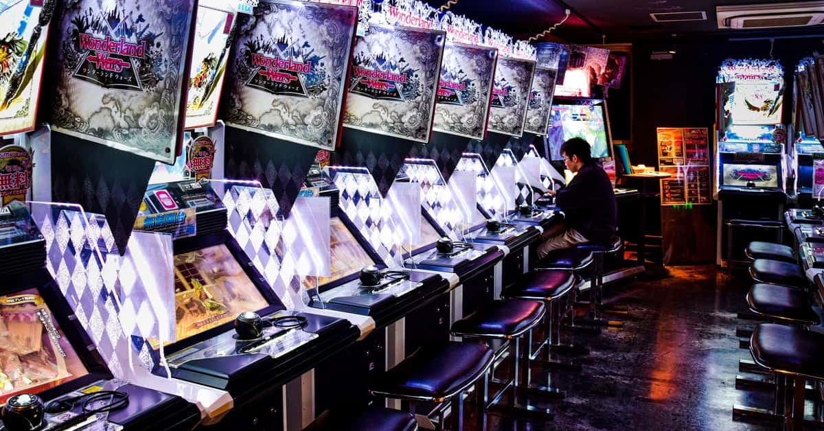 A man plays inside a modern arcade in Tokyo, illuminated by neon lights and gaming machines.