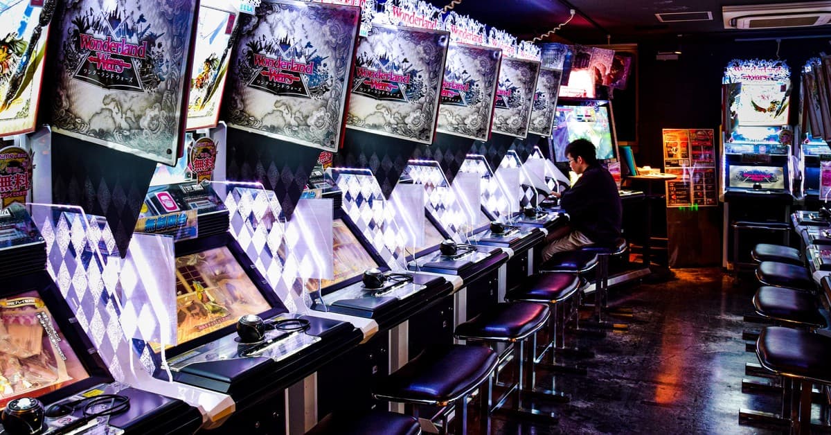 A man plays inside a modern arcade in Tokyo, illuminated by neon lights and gaming machines.