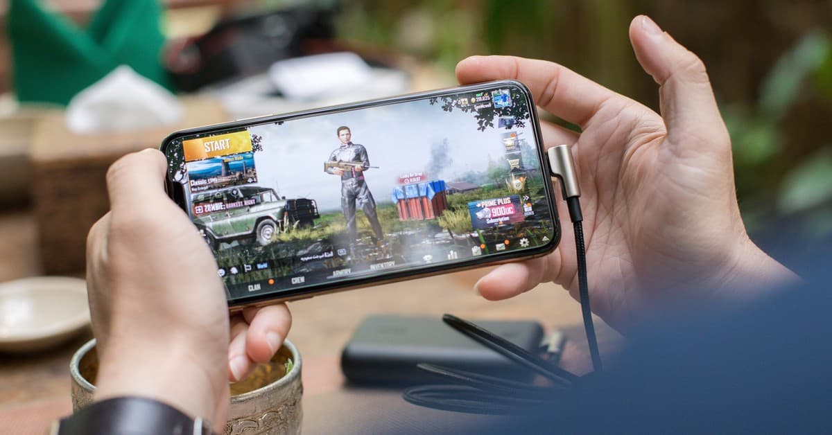 Person playing PUBG on smartphone outdoors with charging cable attached.