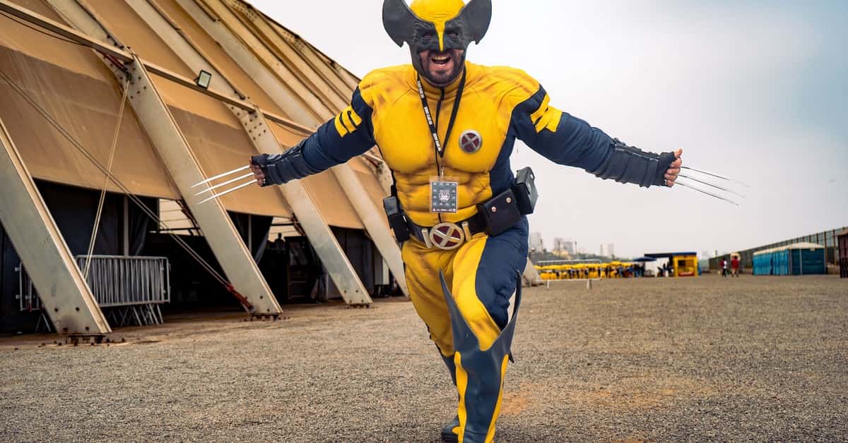 A cosplayer vividly dressed as Wolverine with claws extended outdoors showing excitement.
