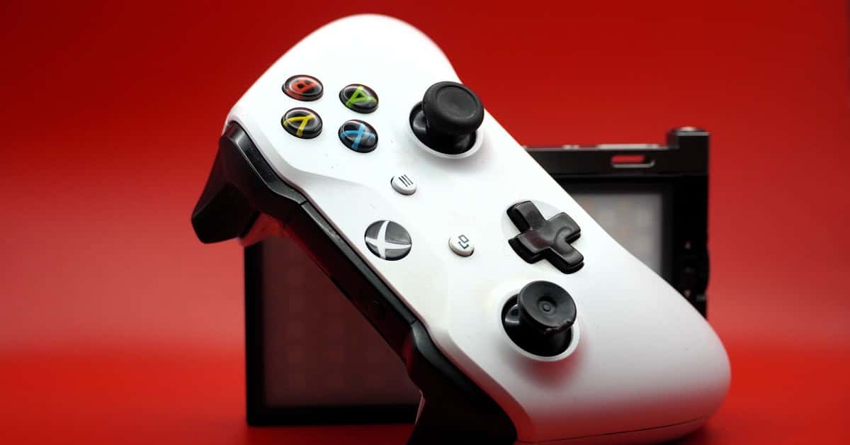 Close-up of a white gaming controller with black buttons against a vivid red backdrop.