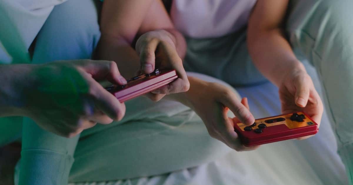 Close-up of a couple's hands holding retro game controllers while gaming indoors.