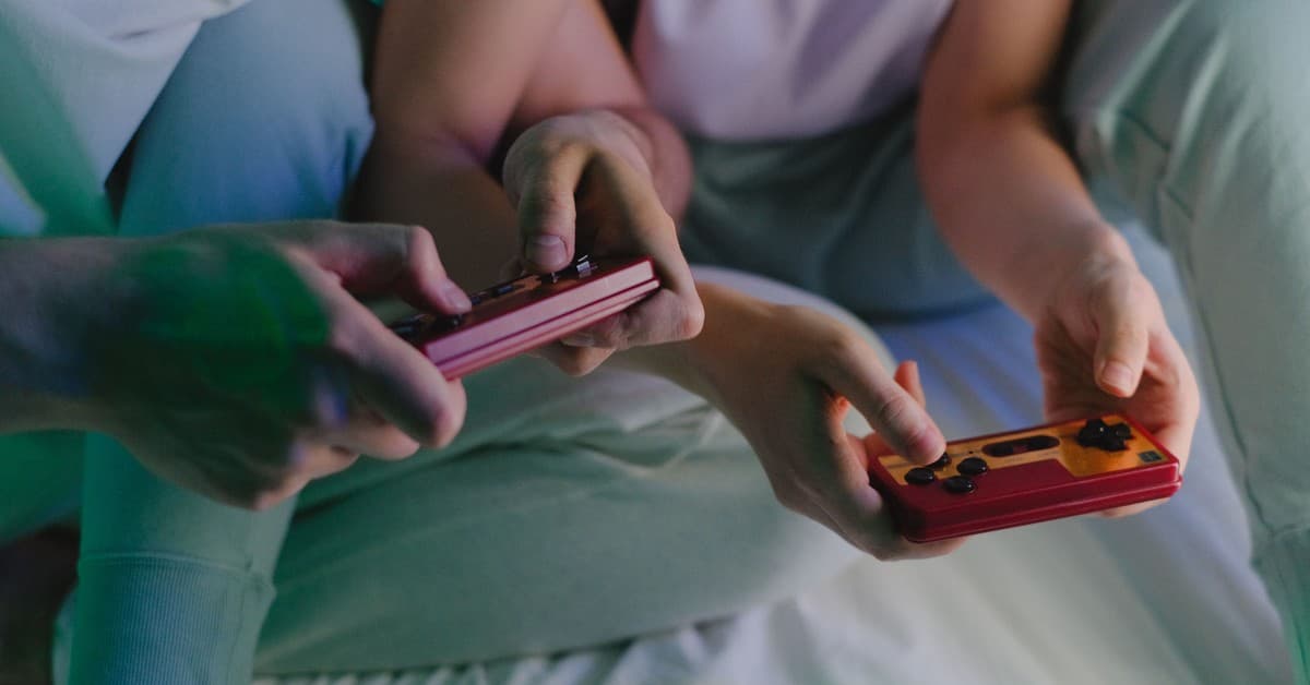 Close-up of a couple's hands holding retro game controllers while gaming indoors.