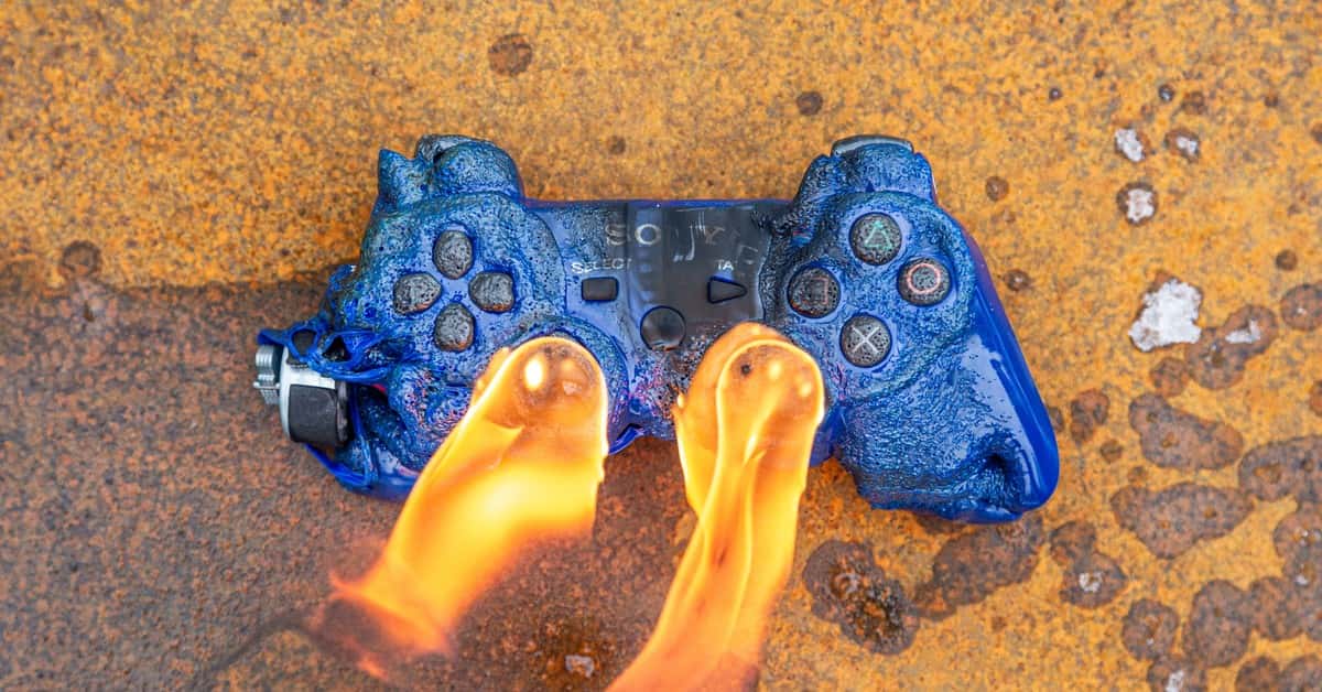 Close-up of a melting blue game controller engulfed in flames on a rusted surface.