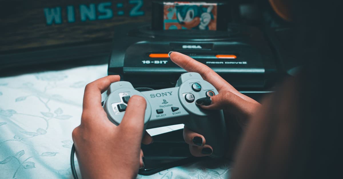 Close-up of hands holding vintage Sony controller with Sega Mega Drive in background.